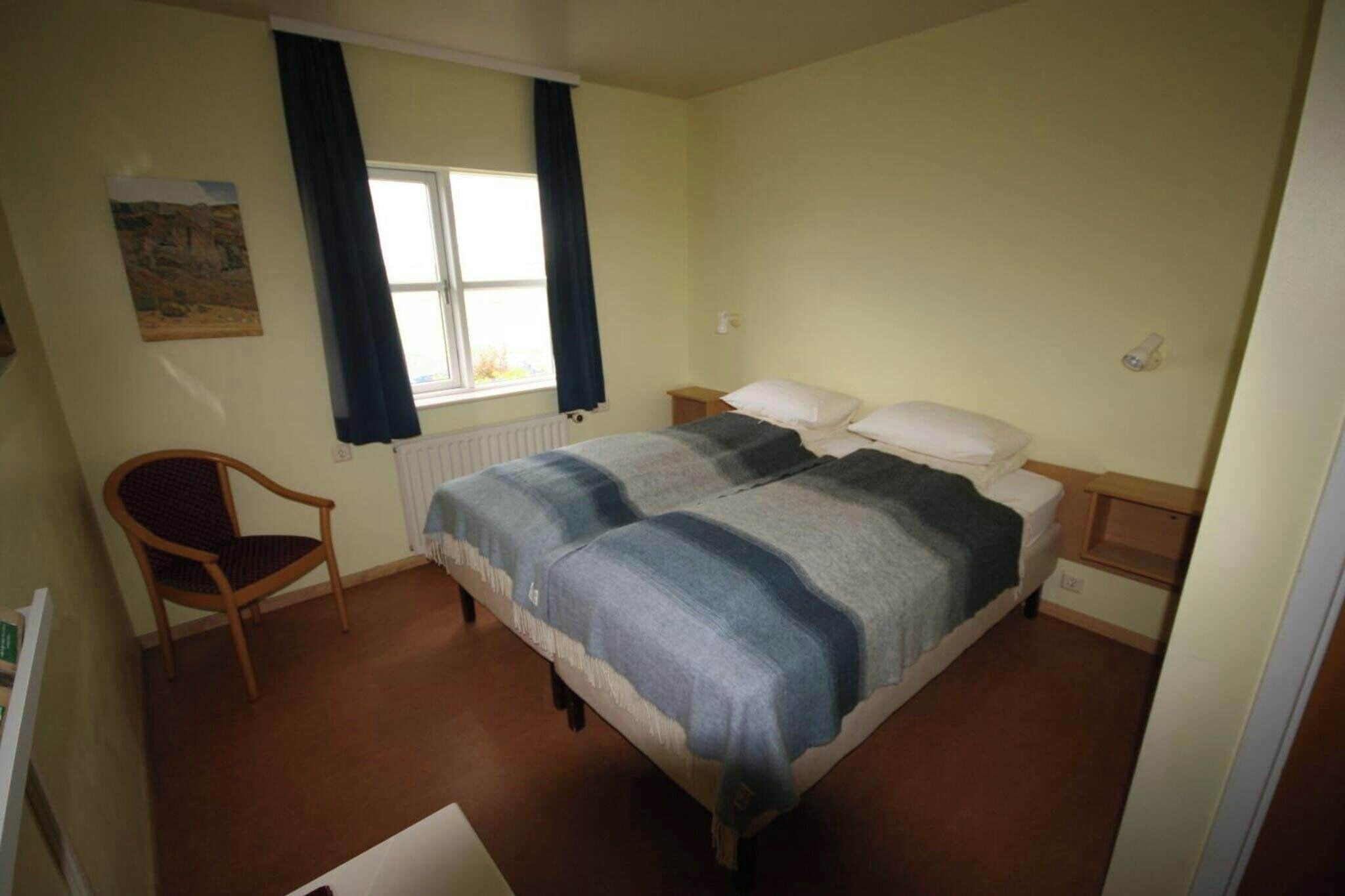 A bedroom with a bed, a chair, a window with curtains, and a radiator.