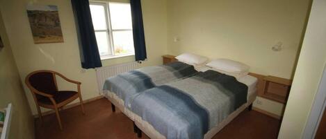 A bedroom with a bed, a chair, a window with curtains, and a radiator.