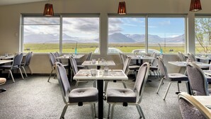 A dining area with tables and chairs, large windows with a mountain view, and pendant lights. - Brunnhóll Country Guesthouse (Höfn)