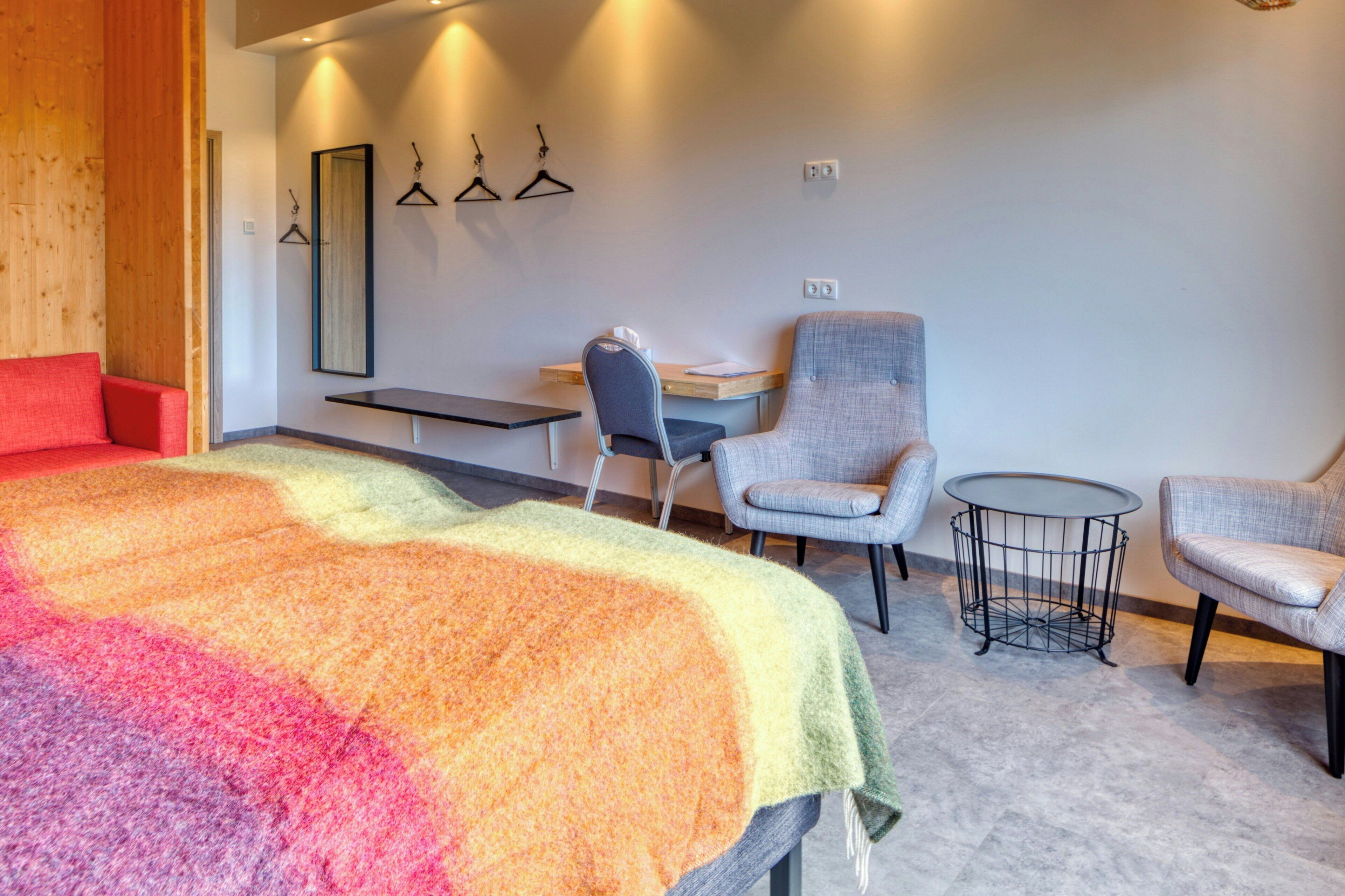 A modern hotel room with a large bed, a desk, two armchairs, and a small round table.