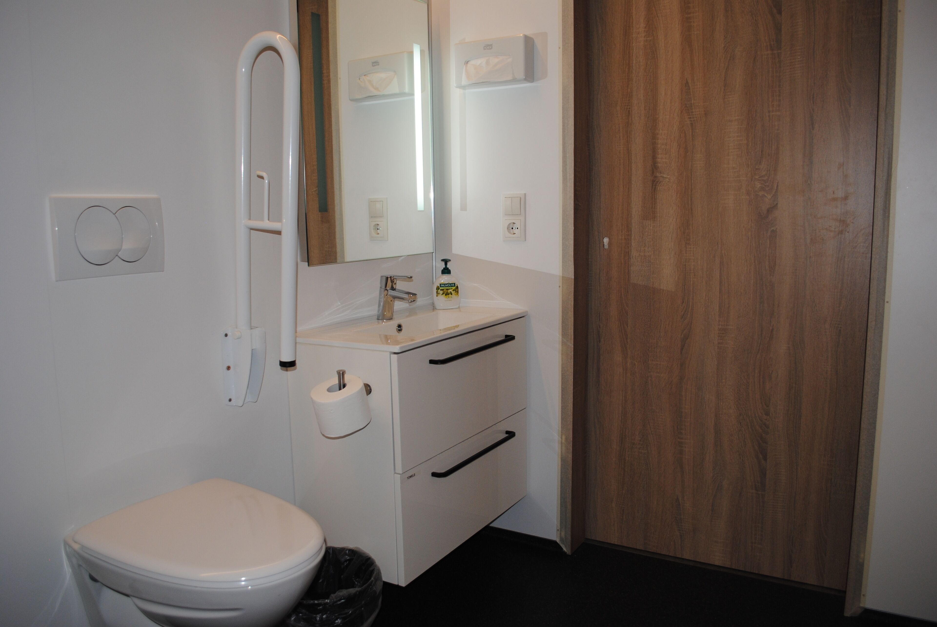 Un baño con inodoro, lavamanos con espejo y puerta de madera.