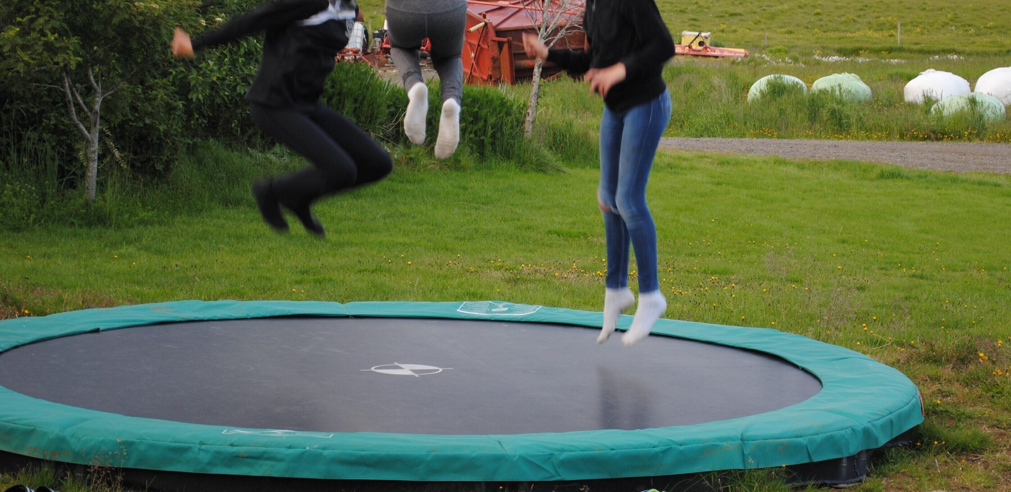 Een trampoline in een gazon met een onverharde pad en hooi-balen op de achtergrond.
