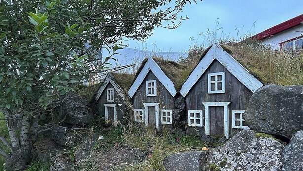 Three rustic wooden houses with gabled roofs, surrounded by rocks and vegetation. - Brunnhóll Country Guesthouse (Höfn)