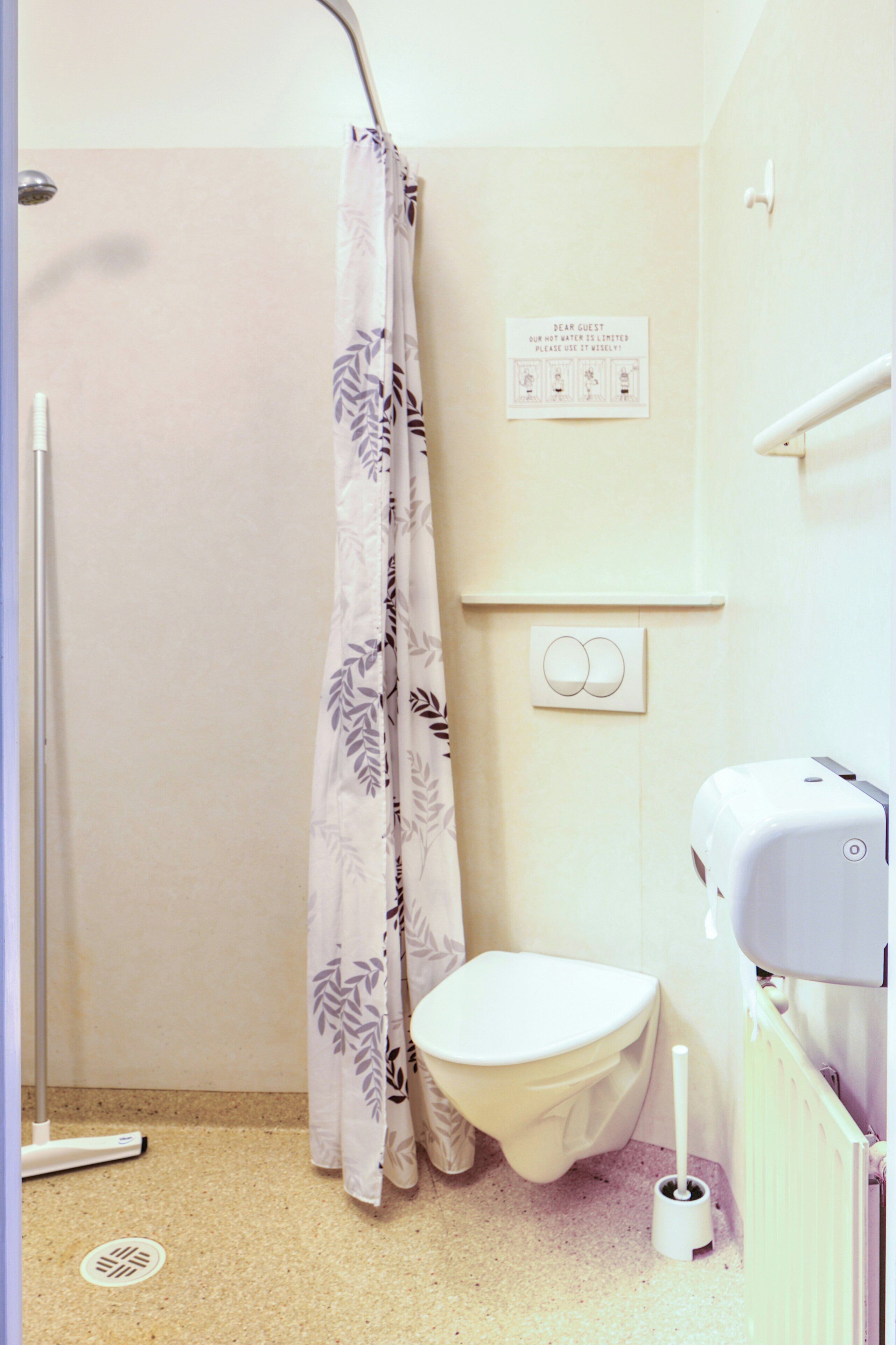 A bathroom with a shower curtain, toilet, bidet, and a sign on the wall.