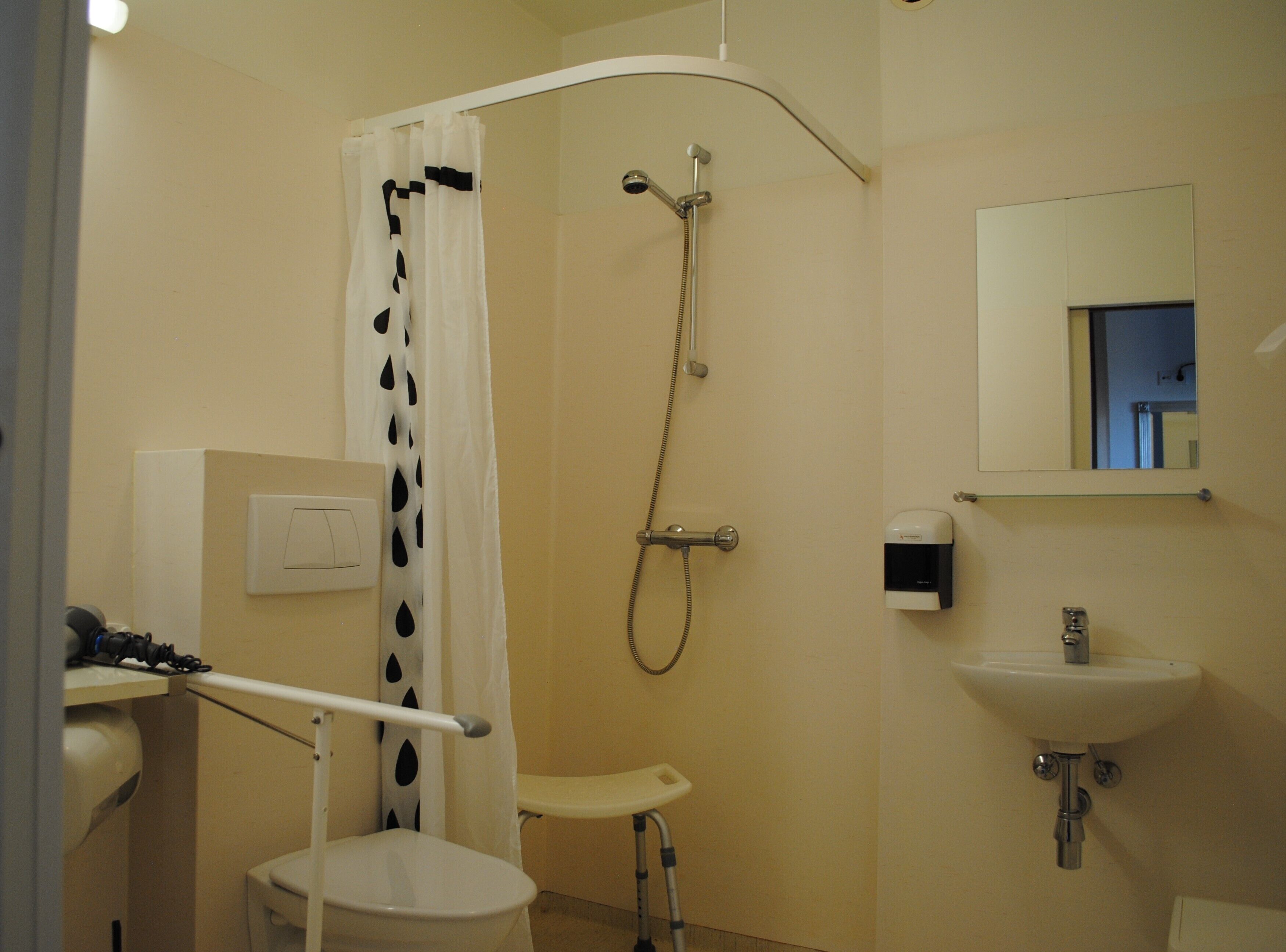 A bathroom with a shower, toilet, sink, and a hand dryer.