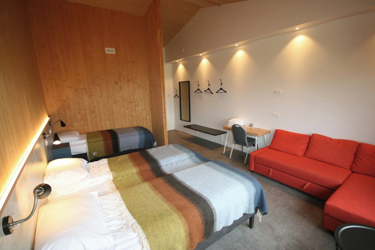 Ein Hotelzimmer mit einem Bett, einem Schreibtisch, einem roten Sofa und einer Holzwand.