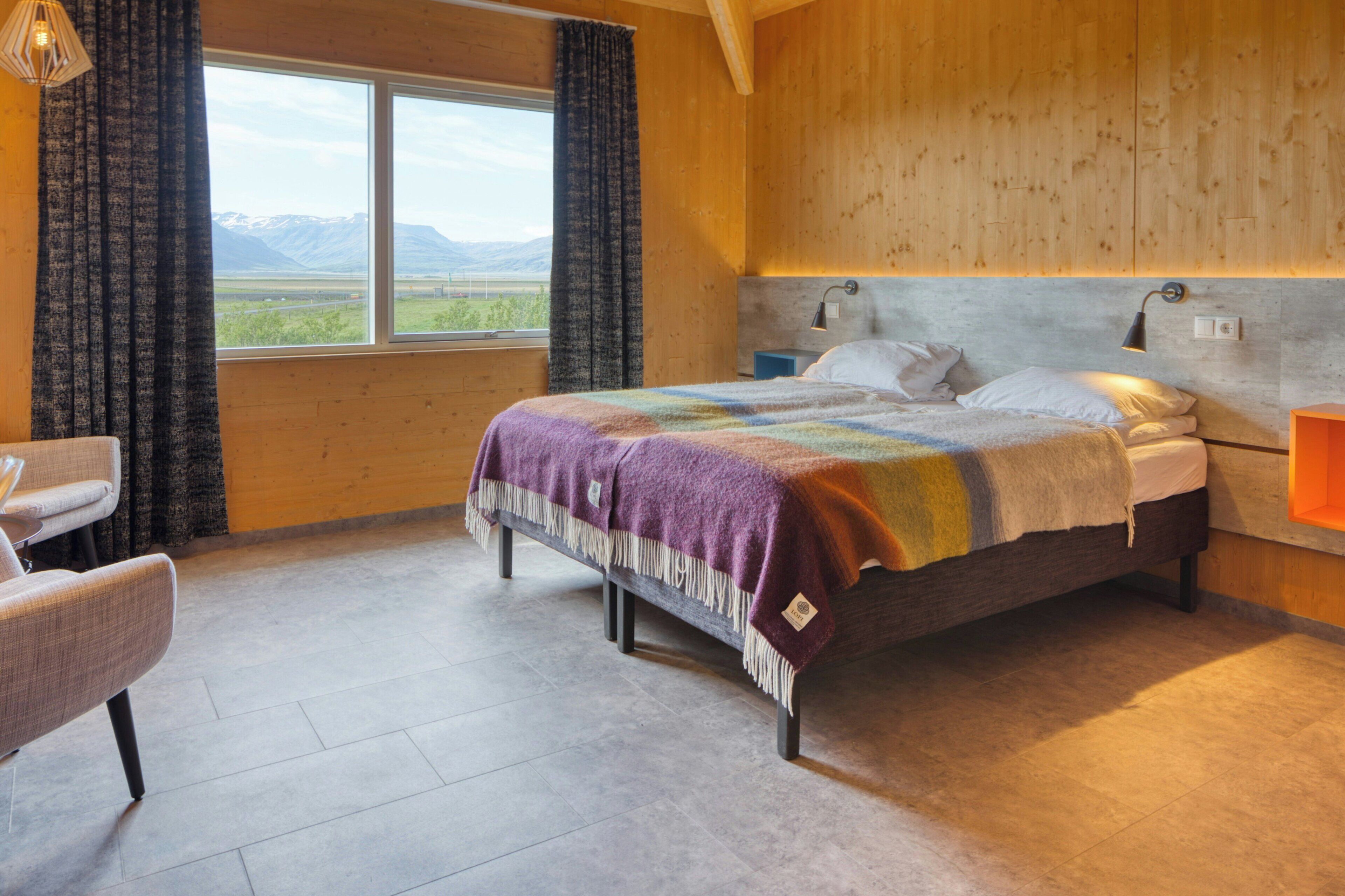 A bedroom with a bed, a chair, a window with curtains, and a view of mountains.