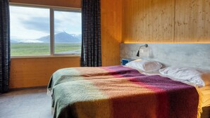 A room with a bed, a window with curtains, a view of mountains, and wooden walls. - Brunnhóll Country Guesthouse (Höfn)