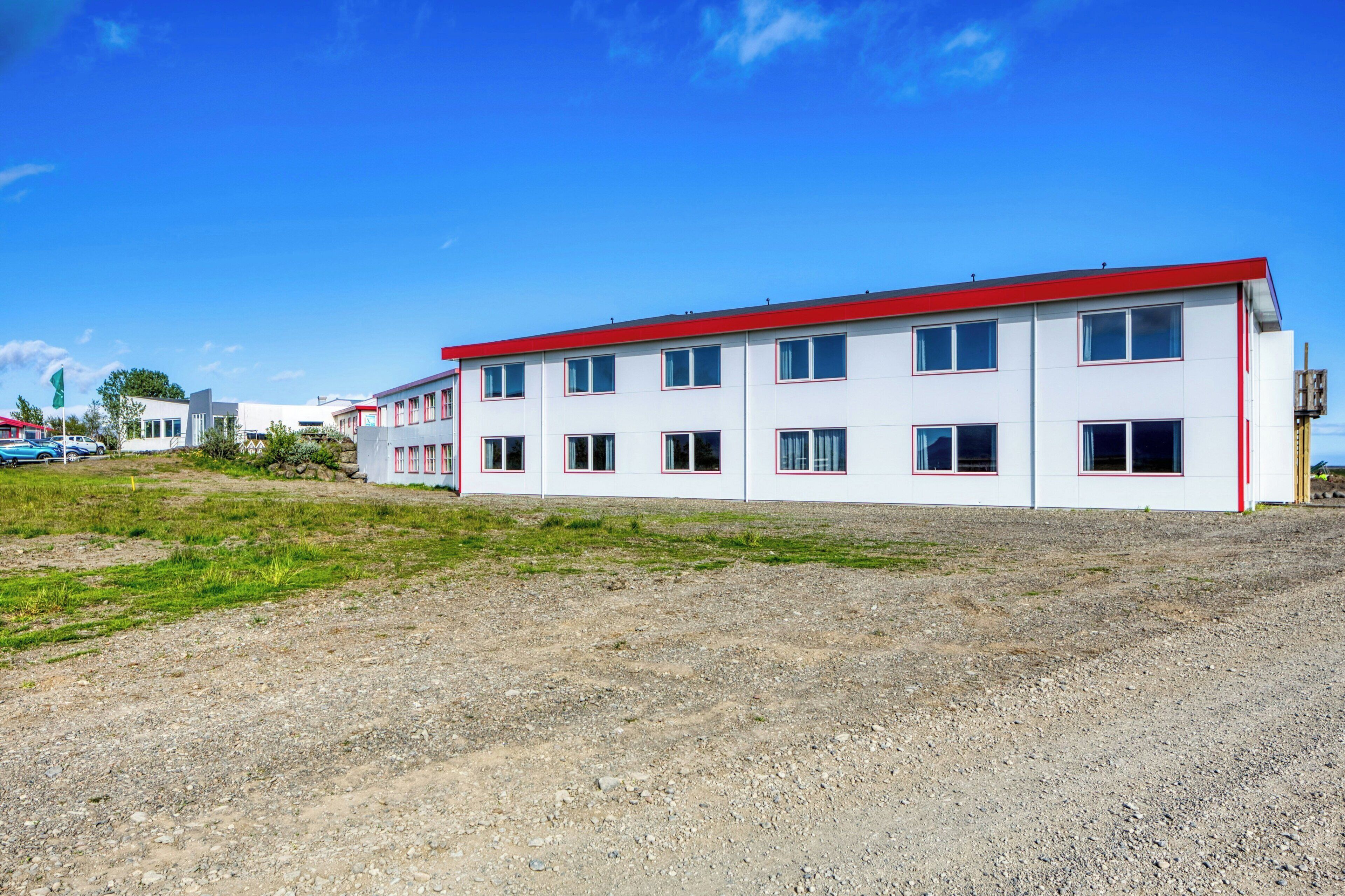 A multi-story building with a red roof and white walls, located in a rural area with a gravel ground.