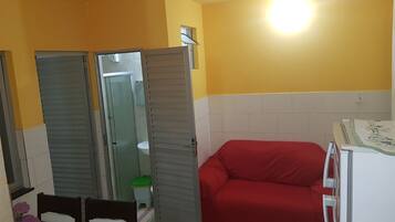 A compact kitchen with a refrigerator, a dining table with chairs, and a red sofa.