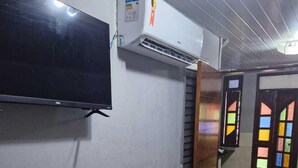 Um corredor com televisão de tela plana fixada na parede, um ar-condicionado e uma porta com vitrais coloridos.