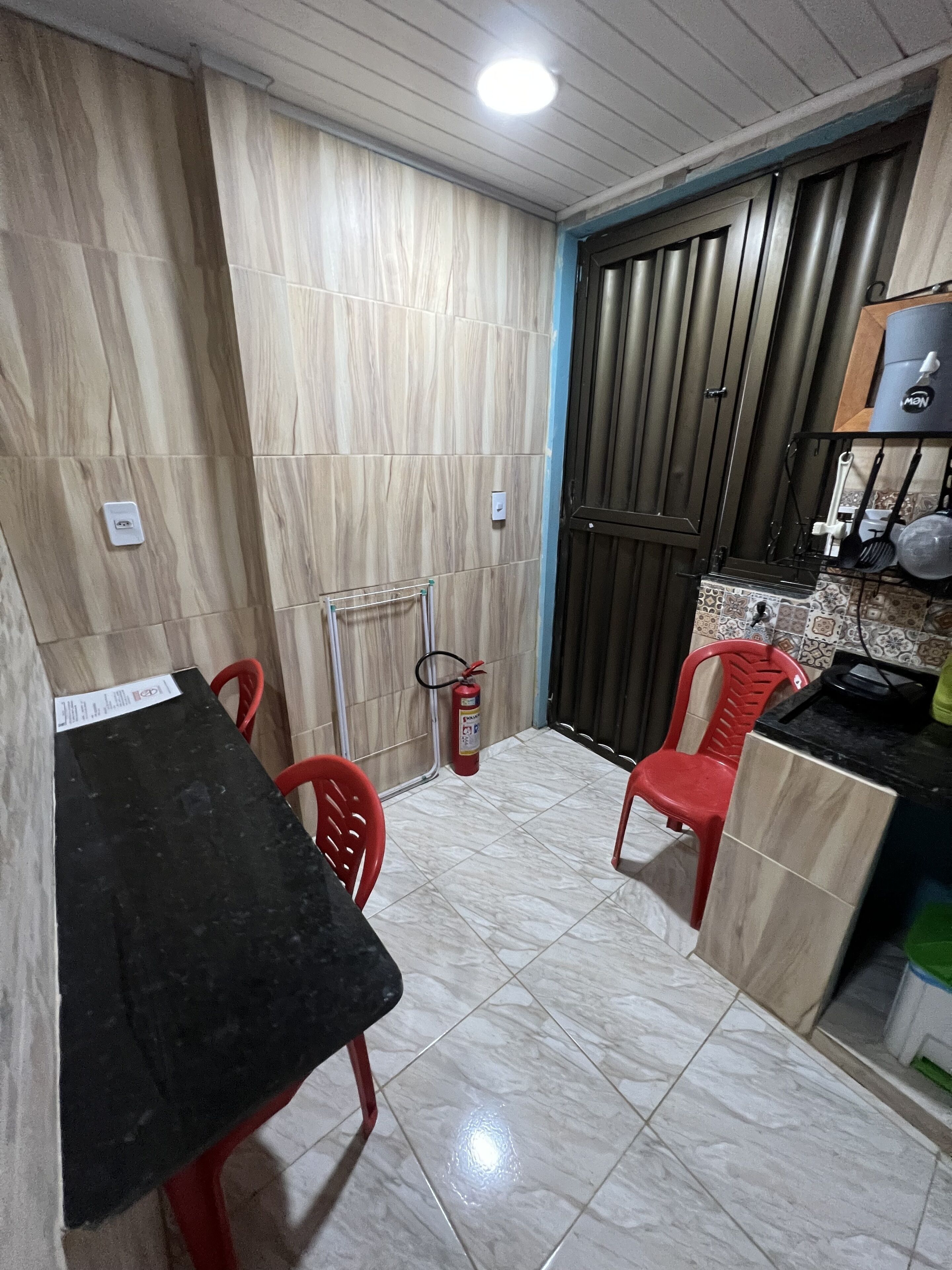 A compact kitchen with a black countertop, red chairs, a fire extinguisher, and a tiled floor.