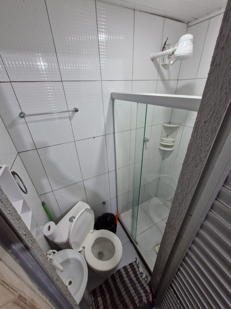 A small, compact bathroom with white tiled walls, a glass shower enclosure, a toilet, a bidet, and a towel rack.