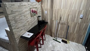 Quarto pequeno e moderno com piso de azulejos, balcão preto, cadeiras vermelhas e um arranjo floral decorativo.