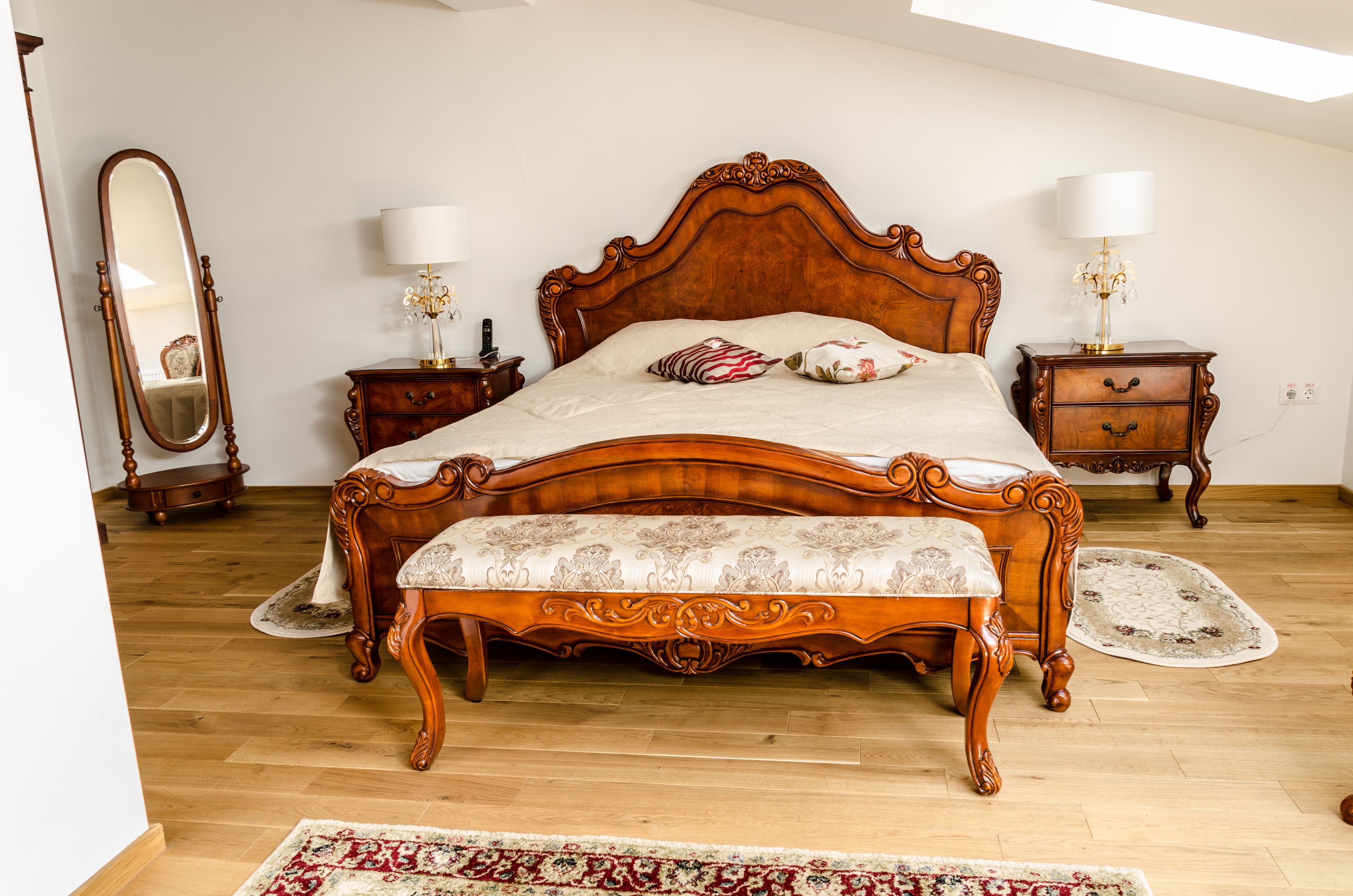 Un dormitorio con una cama de madera grande, dos mesitas de noche con lámparas, un espejo y una alfombra estampada.