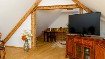 A room with a wooden ceiling, a television on a wooden cabinet, a vase with flowers, and a dining table with chairs.