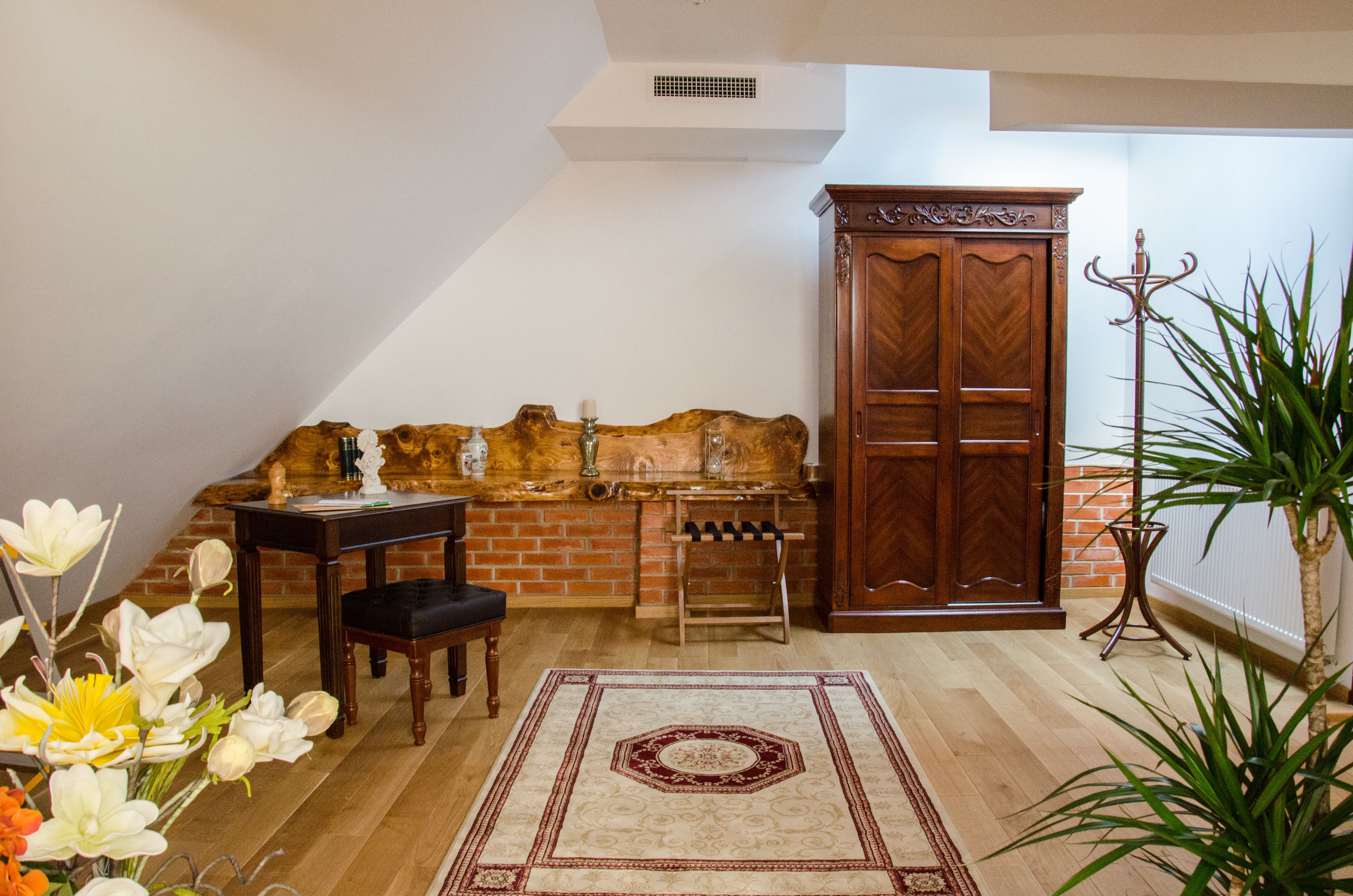 Una habitación con un armario de madera, una mesita con una silla, un radiador y una planta en maceta.
