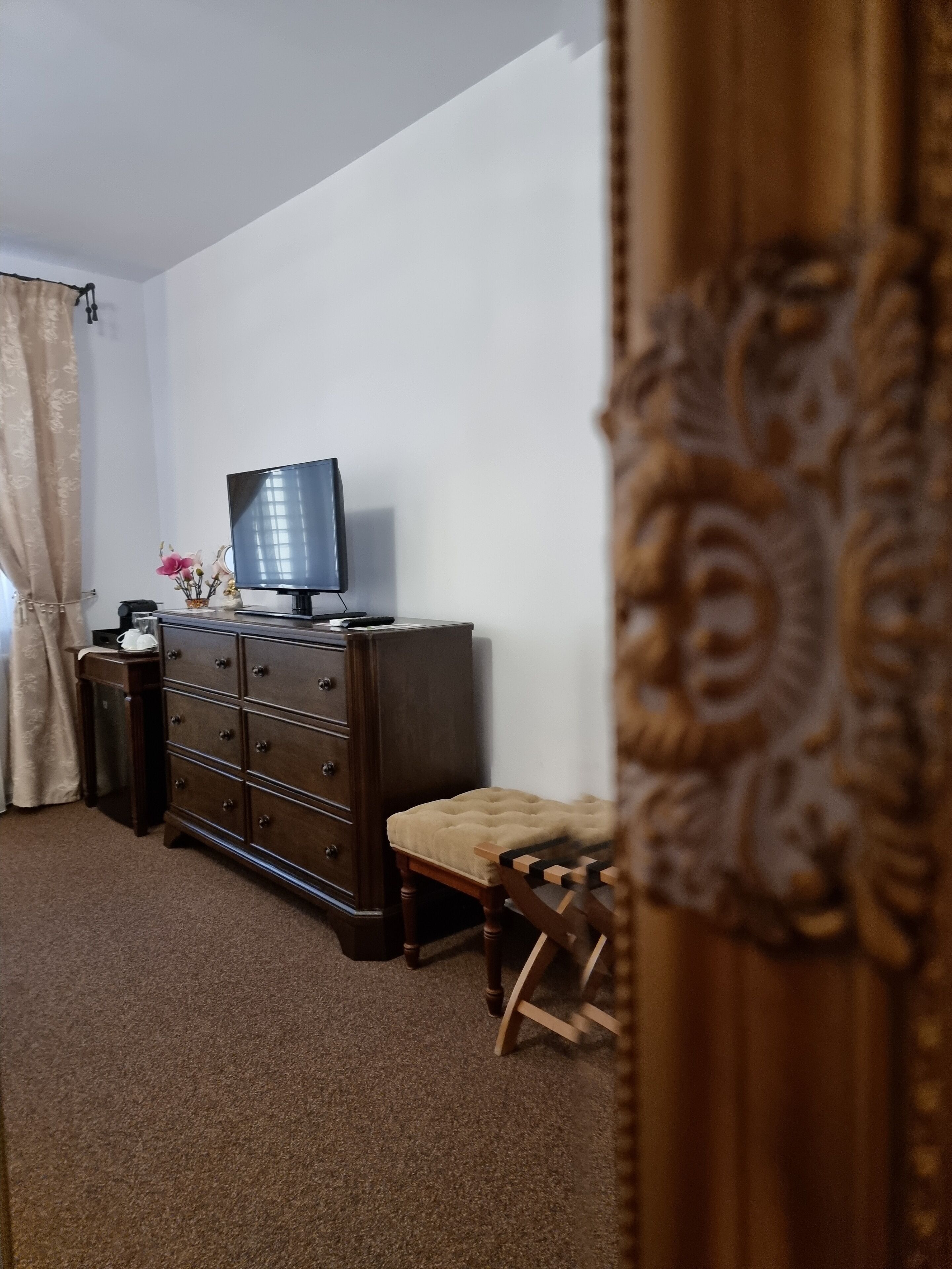 Une pièce avec une commode en bois foncé, un téléviseur posé dessus, un petit banc et un rideau décoratif.