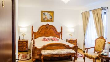 A classic wooden four-poster bed with a bench, two bedside tables with lamps, a chair, and a painting on the wall.