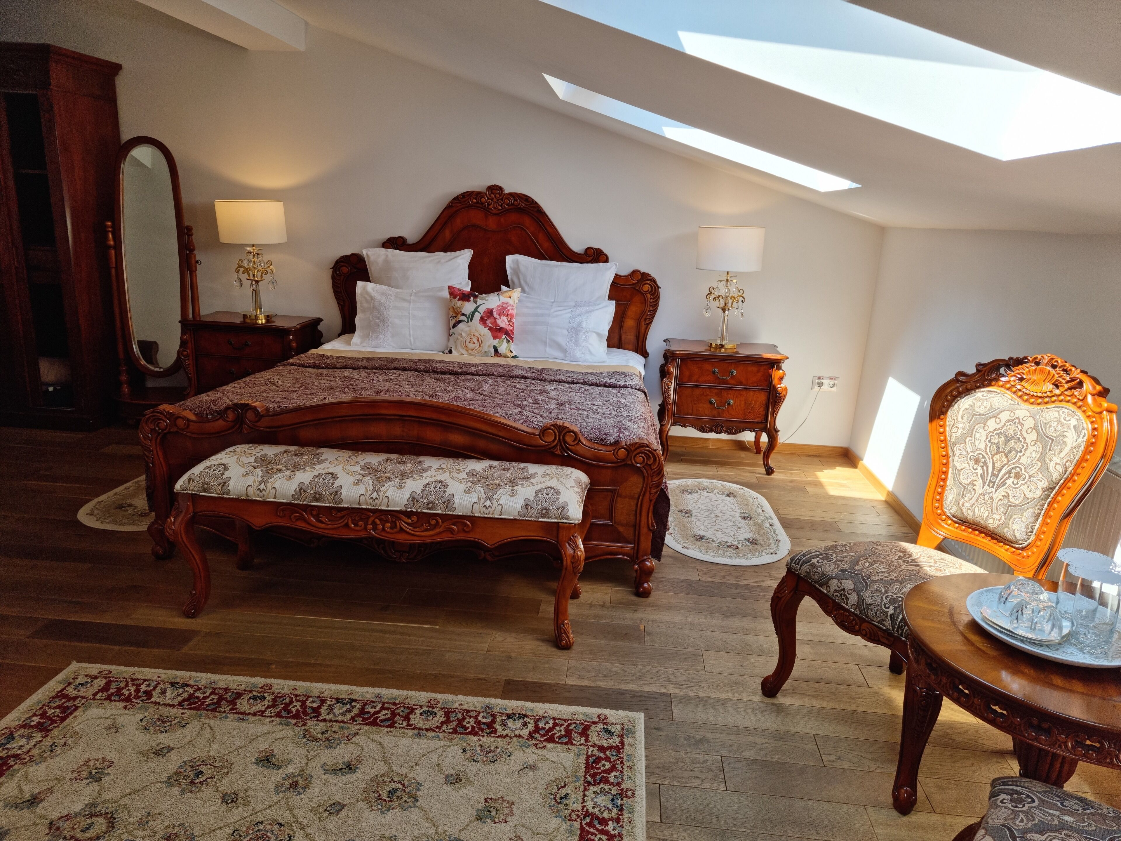 A bedroom with a large bed, a wooden nightstand, a chair, and a table with a tray.