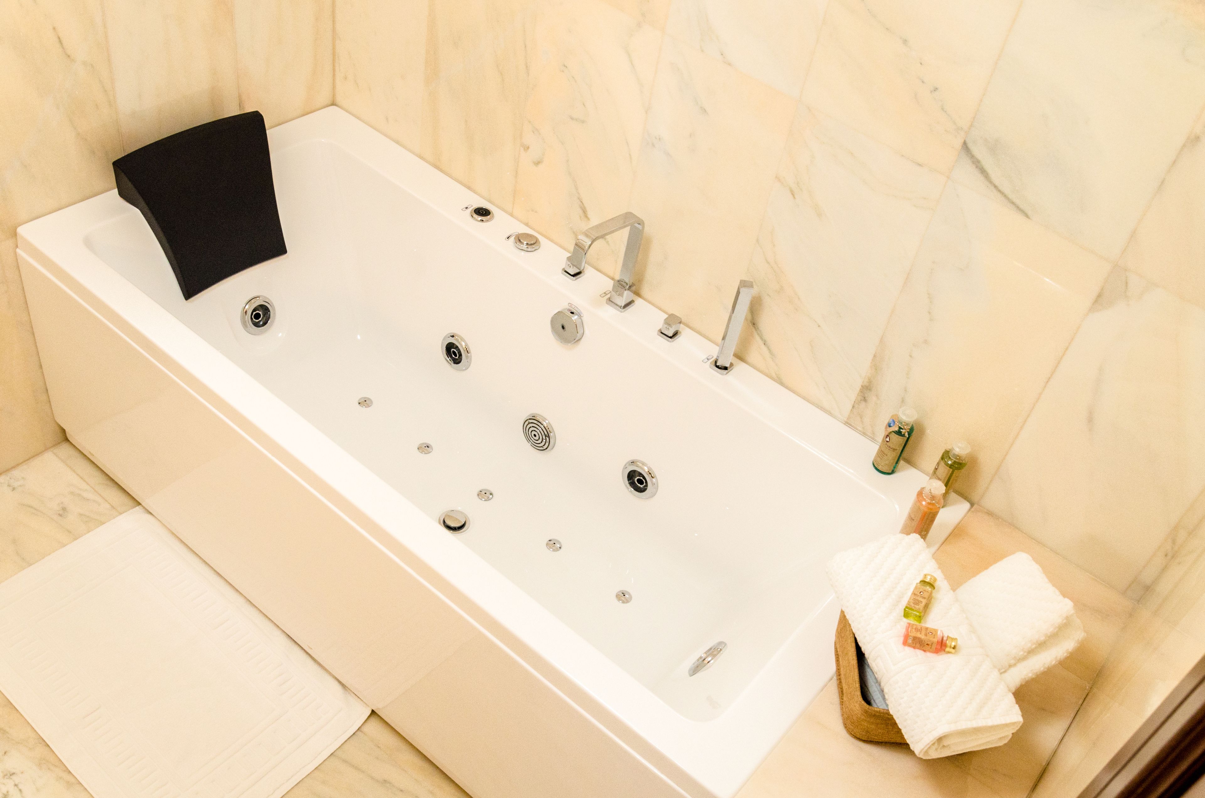 Un baño moderno con una bañera grande, un jabonera negra y una bandeja de madera con una toalla y artículos de aseo.
