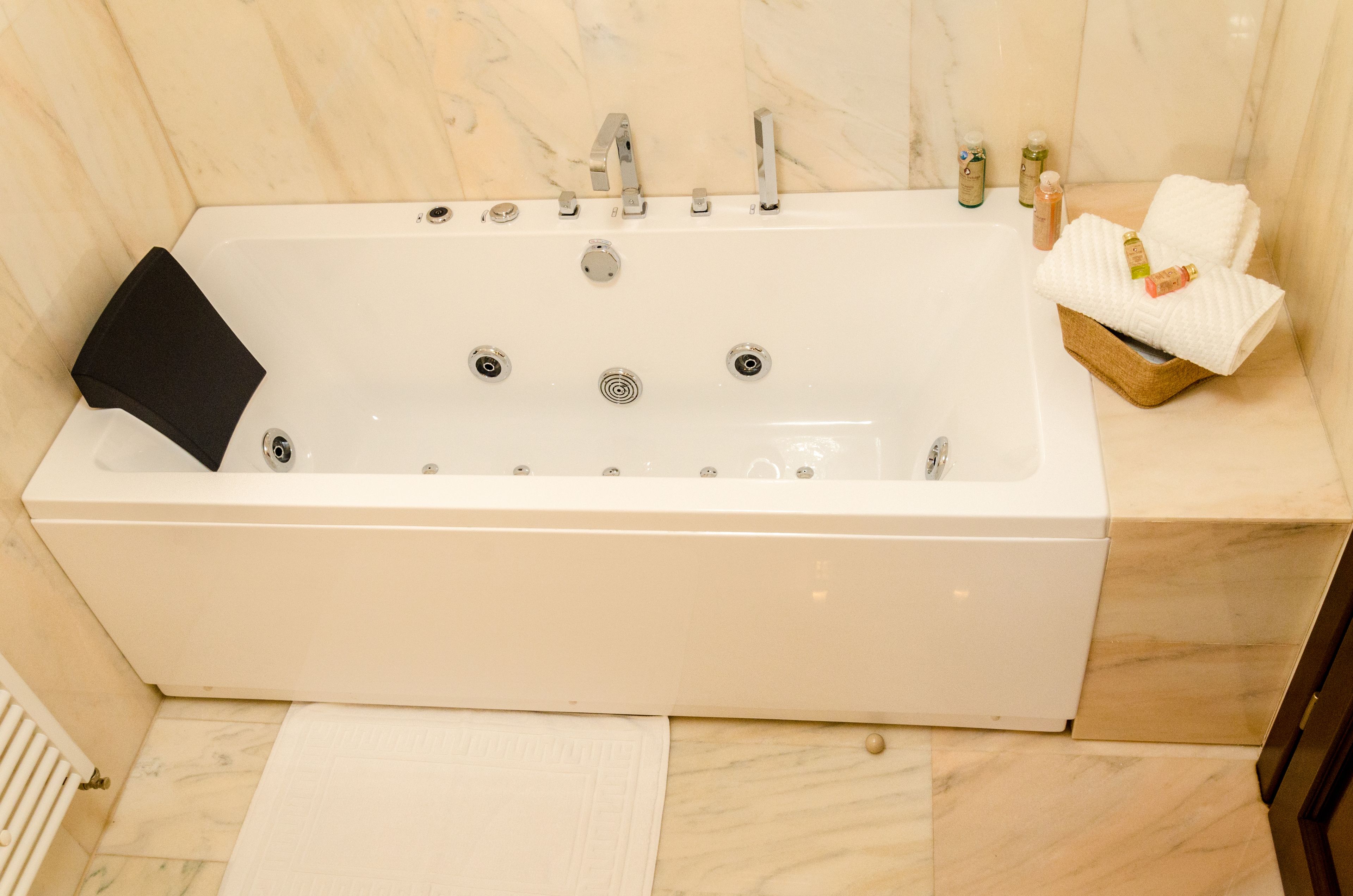 Une salle de bain moderne avec une grande baignoire, un tapis de bain noir, un panier en bois contenant des serviettes et des articles de toilette placés sur le côté.