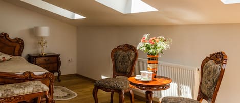 Een slaapkamer met dakraam, een bed, twee stoelen, een tafeltje met een bloevas en een nachtkastje met een lamp.