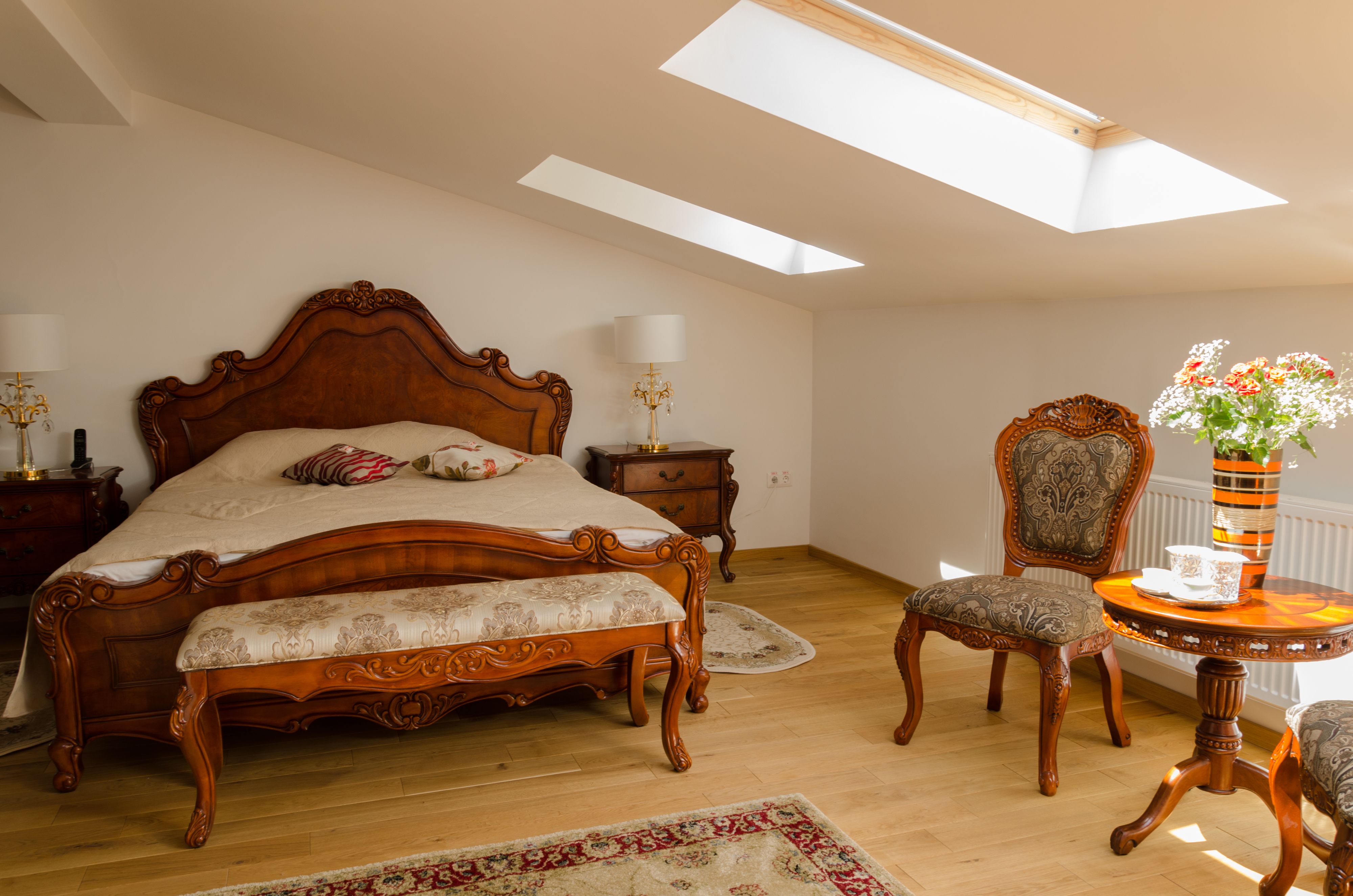 Un dormitorio con una cama grande, una silla, una mesita y un tragaluz.