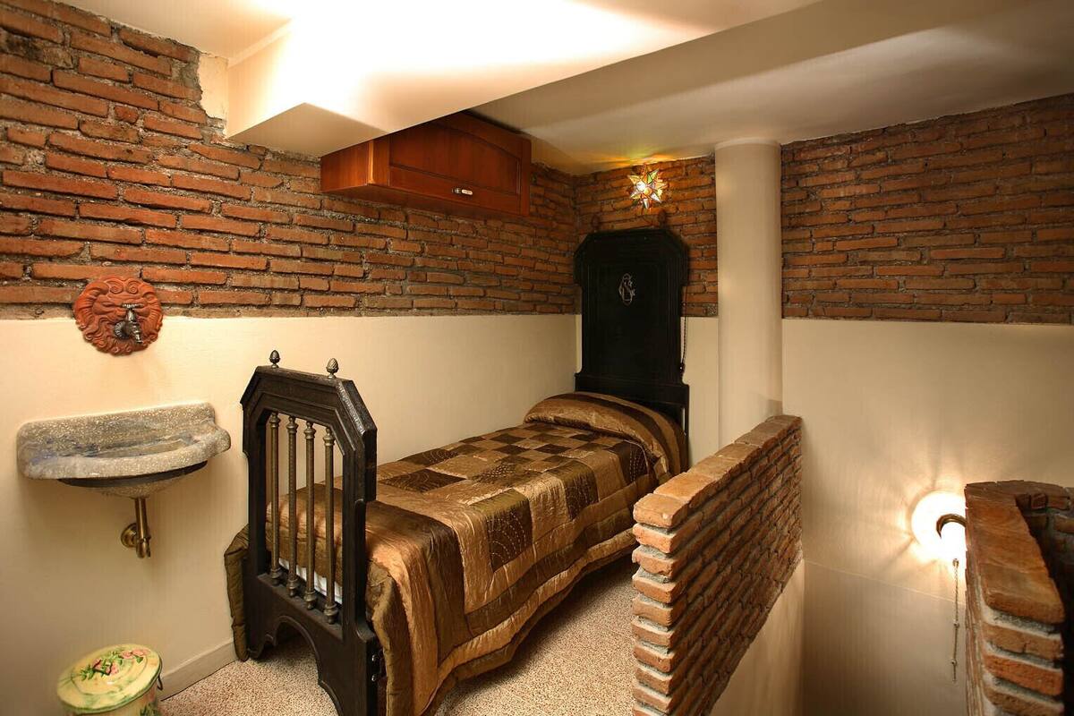 A small, cozy room with a brick wall, a wooden bed, a small sink, and a decorative star-shaped light fixture.