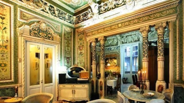 Una habitació ricament decorada amb columnes ornamentals, un penjallum i una taula de dinar preparada per a quatre.
