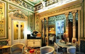 A richly decorated room with ornate columns, a chandelier, and a dining table set for four. - B&B Il Caravaggio (Catania)