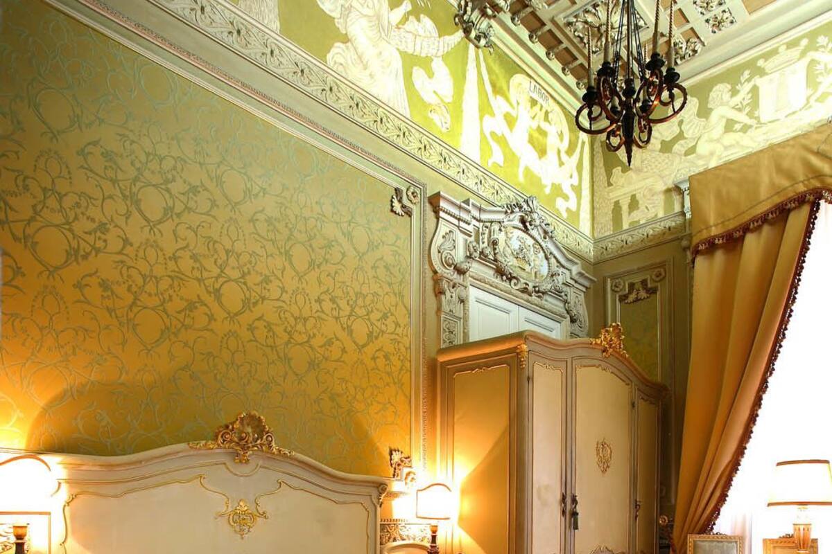 A large, ornate bed with a quilted cover in a room with elaborate wall and ceiling decorations, including a chandelier.