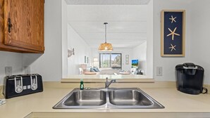 A modern kitchen with a double sink, a toaster, a coffee maker, and a view into the living area. - Poolside St. Augustine Condo – Walk to Beach, Sleeps 4 (St. Augustine)