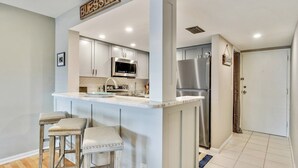 A modern kitchen with a bar area, stainless steel appliances, and a white color scheme. - St. Augustine Ocean & Racquet Getaway – Balcony Overlooking the Sea (St. Augustine)