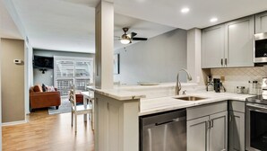 A modern kitchen with a dishwasher, stainless steel appliances, and a dining area with a white table and chairs. - St. Augustine Ocean & Racquet Getaway – Balcony Overlooking the Sea (St. Augustine)