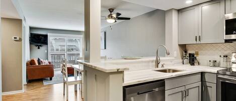 A modern kitchen with a dishwasher, stainless steel appliances, and a dining area with a white table and chairs.