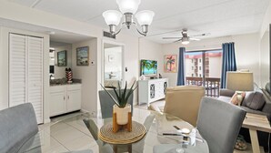 Een moderne woonkamer met een glazen eettafel, grijze banken, een plafondventilator en een televisie op een witte kast.