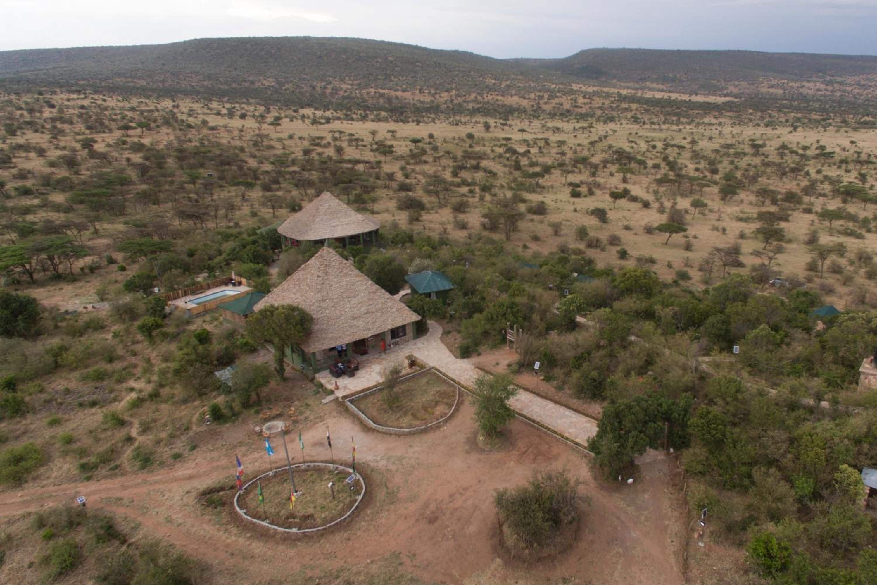 A rural accommodation with a thatched-roof structure, a swimming pool, and a fenced garden area.