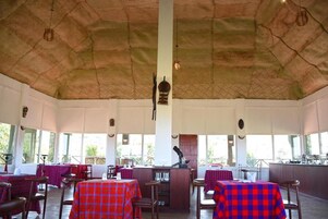 Un comedor interior con mesas cubiertas de manteles a cuadros rojos y azules, sillas de madera y un techo alto con diseño texturizado.