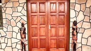 A wooden double door with a stone-patterned wall and two statues on either side. - La Maison Royale Masai Mara (Maasai Mara)