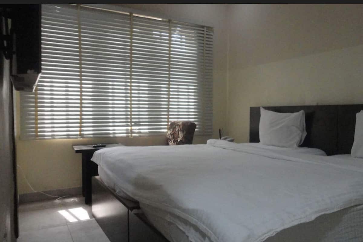 A bedroom with a large bed, a nightstand, a chair, and a window with blinds.