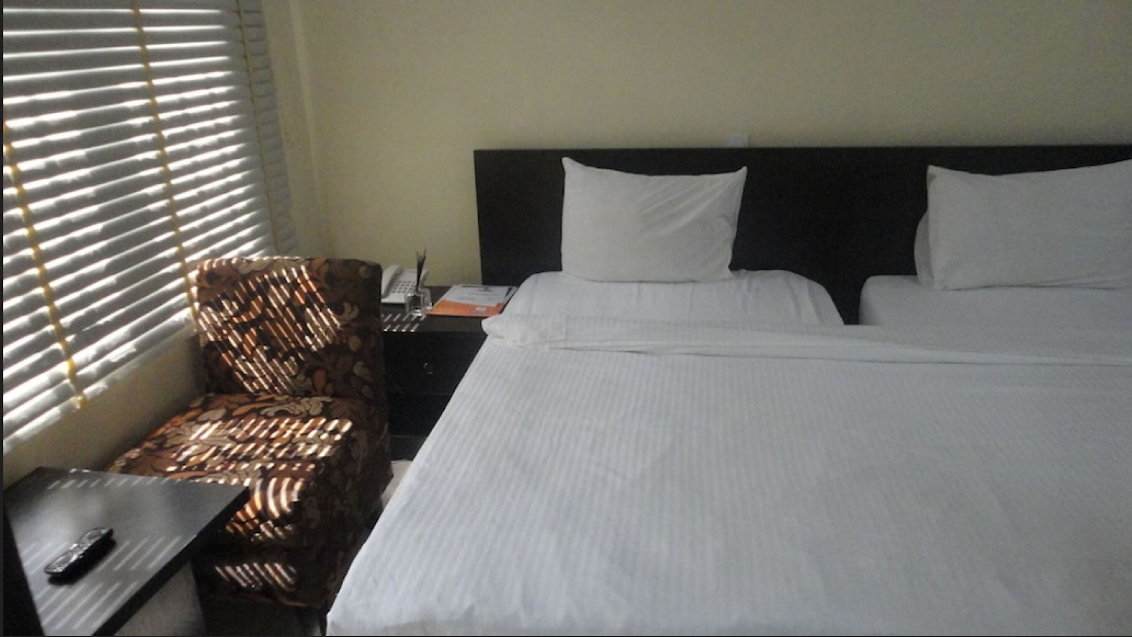 A hotel room with a bed, a nightstand, a chair, and a window with blinds.