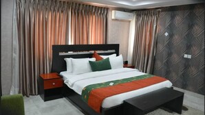 Una habitación de hotel moderna con una cama grande, una mesita de noche, un banco y un papel tapiz estampado.