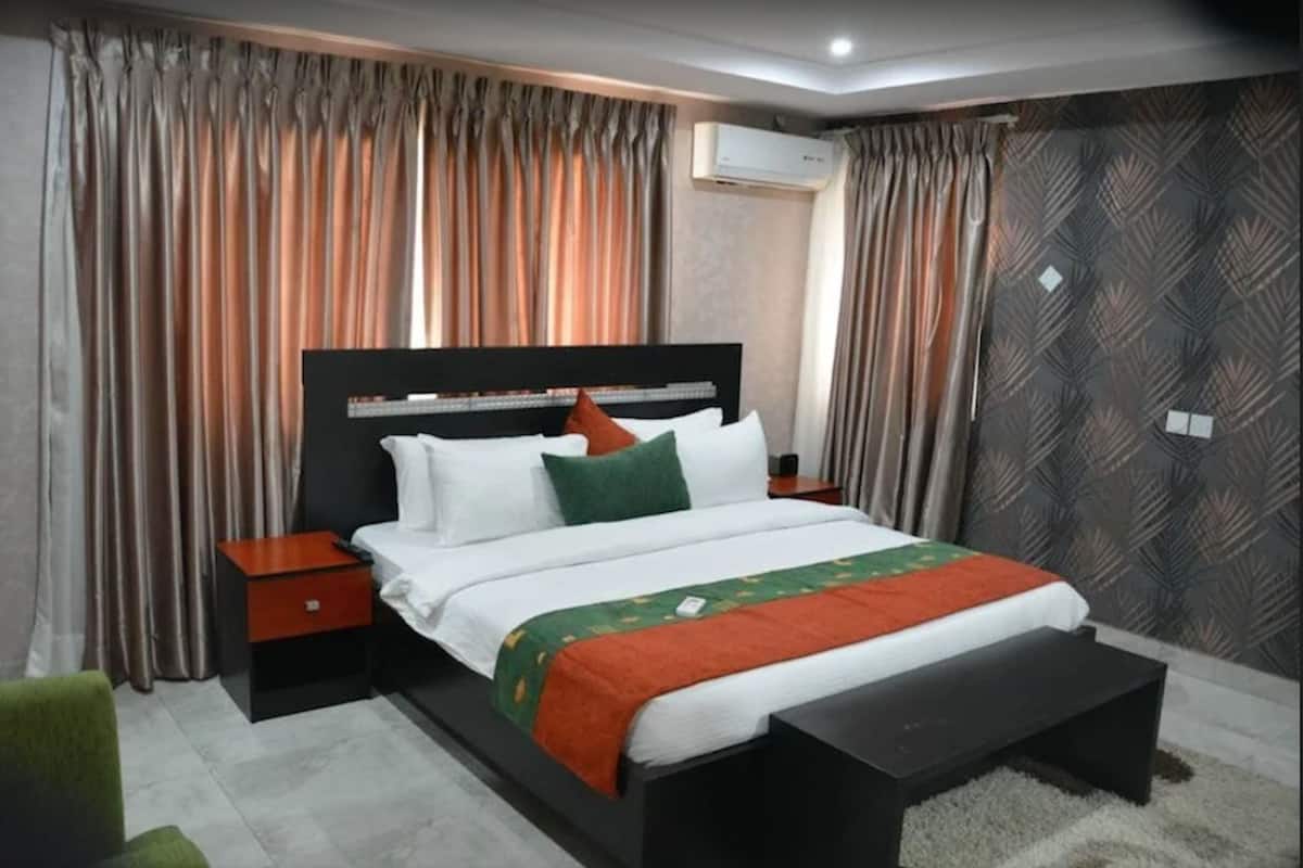 A modern hotel room with a large bed, a bedside table, a bench, and a patterned wall.