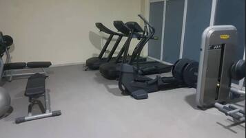 Une salle de sport équipée de tapis de course, d’appareils de musculation et d’un banc.
