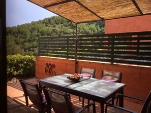 An outdoor patio with a table set for dining, surrounded by chairs, and a view of a forested hillside. - 3 bedroom semi-detached house in Sa Riera, Begur. Sea views, terrace and shared pool (Ref:H12) (Begur)