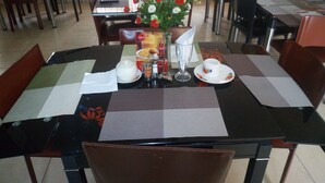 A dining area with tables set for meals, featuring placemats, cutlery, and a vase with flowers. - Peak Court Hotels (Ibadan)
