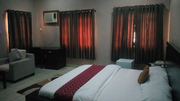 A hotel room with a large bed, a sofa, a desk, and curtains. - Peak Court Hotels (Ibadan)