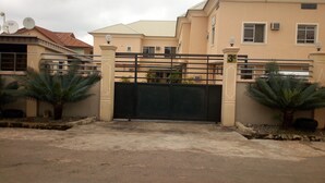 A gated residential area with a beige building, a metal gate, and two palm trees. - Peak Court Hotels (Ibadan)