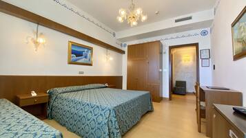 A hotel room with two beds, a desk, a wardrobe, and a chandelier.